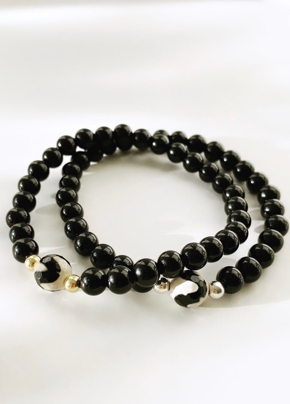 A beaded bracelet made of black onyx stones with a central agate gemstone bead, featuring gold or silver accent beads