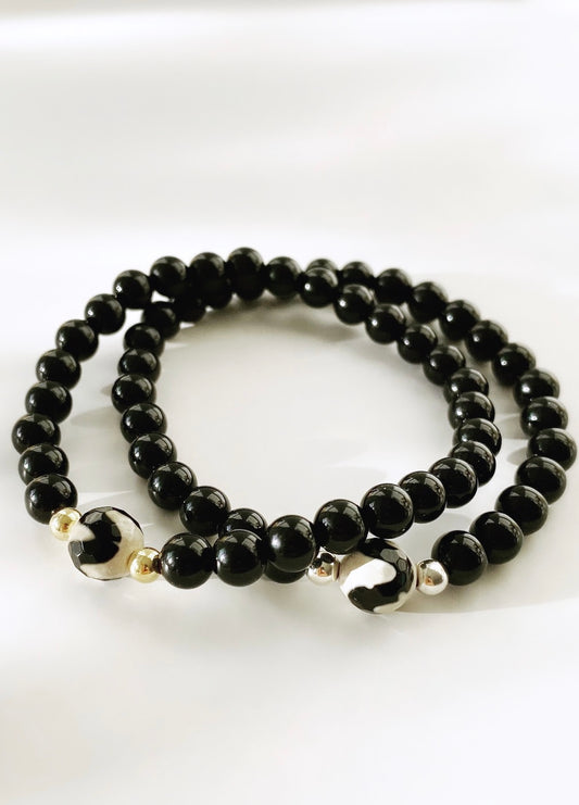 A beaded bracelet made of black onyx stones with a central agate gemstone bead, featuring gold or silver accent beads