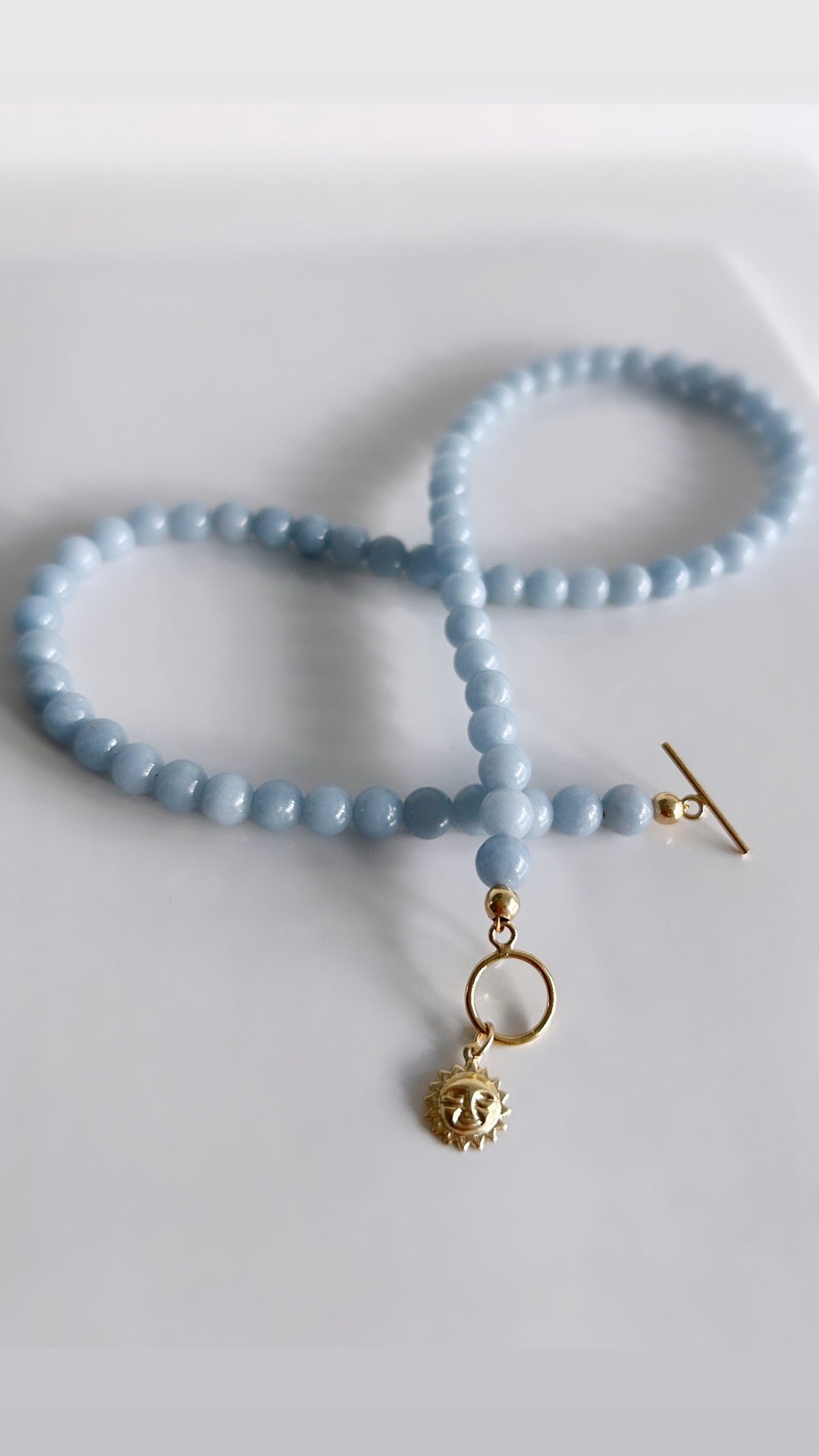 A beautiful baby blue Angelite necklace, with a glorious Gold filled Sun face charm - a perfect Summer accessory! 

The necklace measures approximately 16” in length. The Gold sun charm measures 8mm, and the necklace is finished with a Gold filled lobster clasp. 