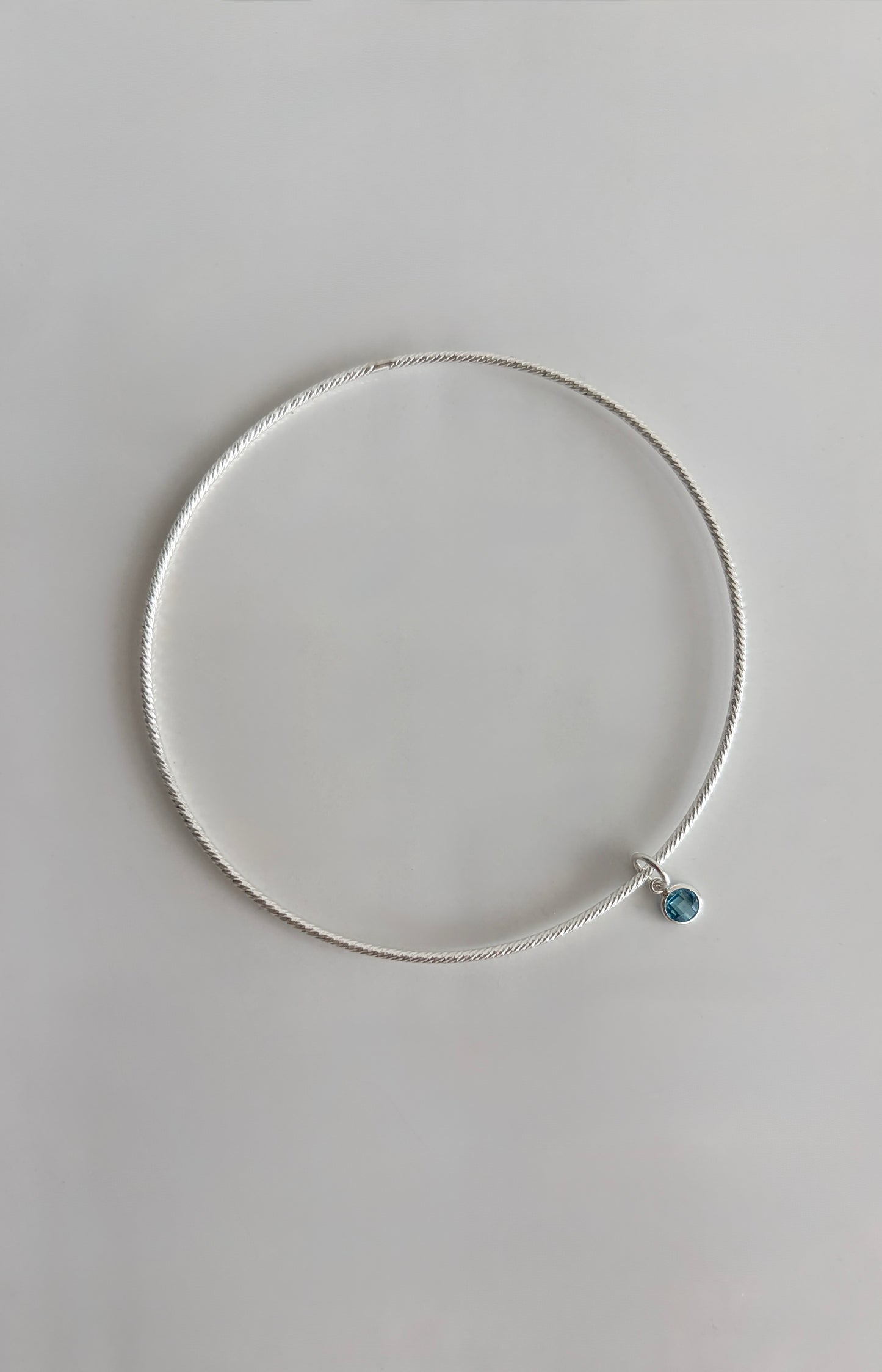 A beautiful Sterling Silver bangle, made with a sparkle finish adorned with your choice of a single crystal Birthstone charm  