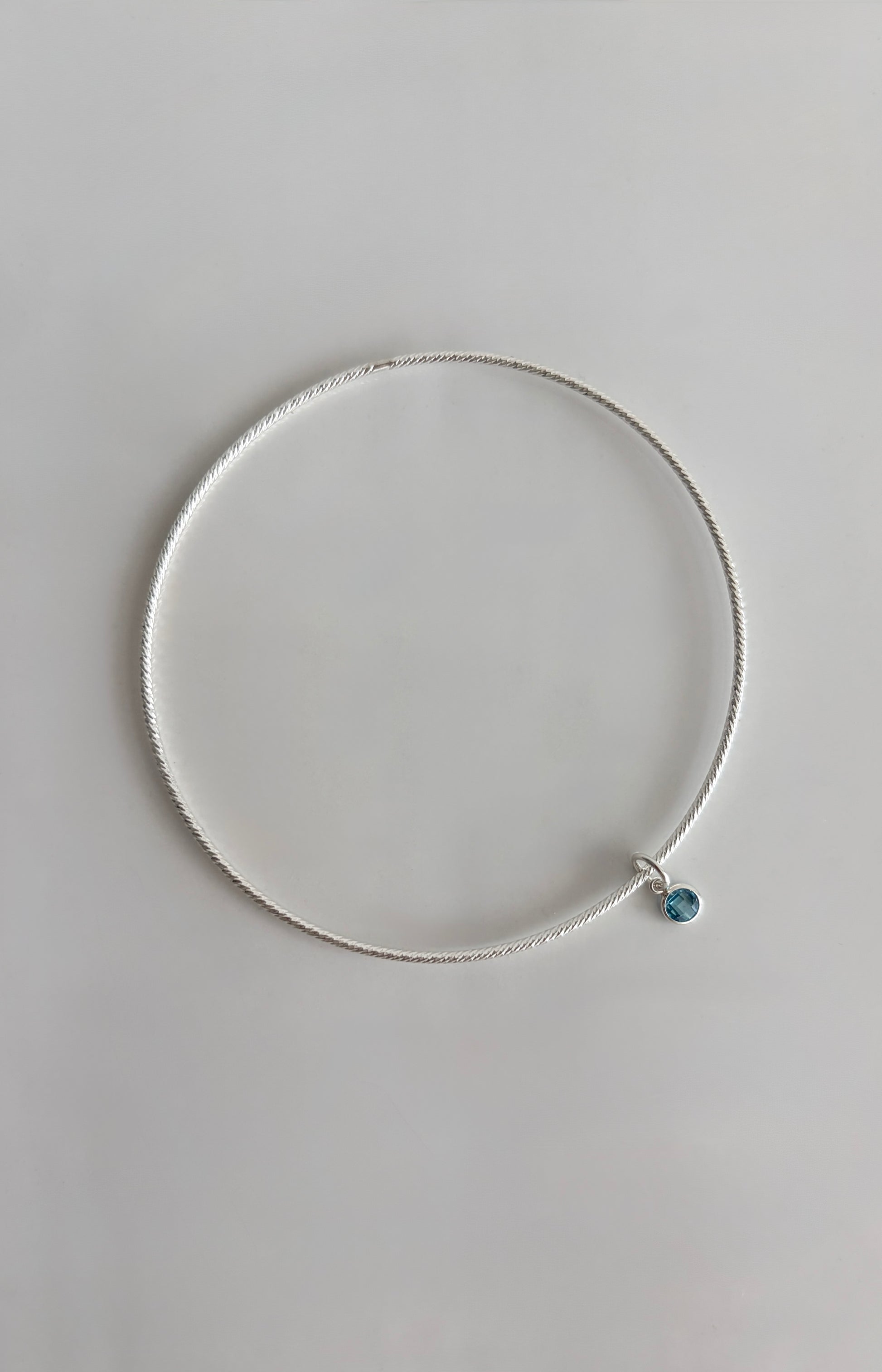 A beautiful Sterling Silver bangle, made with a sparkle finish adorned with your choice of a single crystal Birthstone charm  