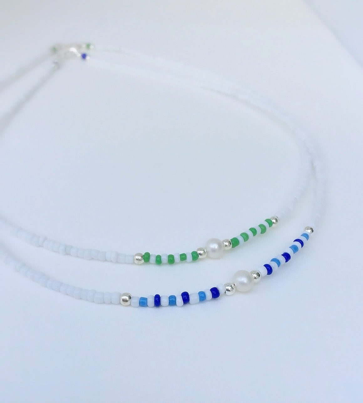 Two seed bead necklaces, one with blue beads and the other with green, both interspersed with silver beads and white pearls