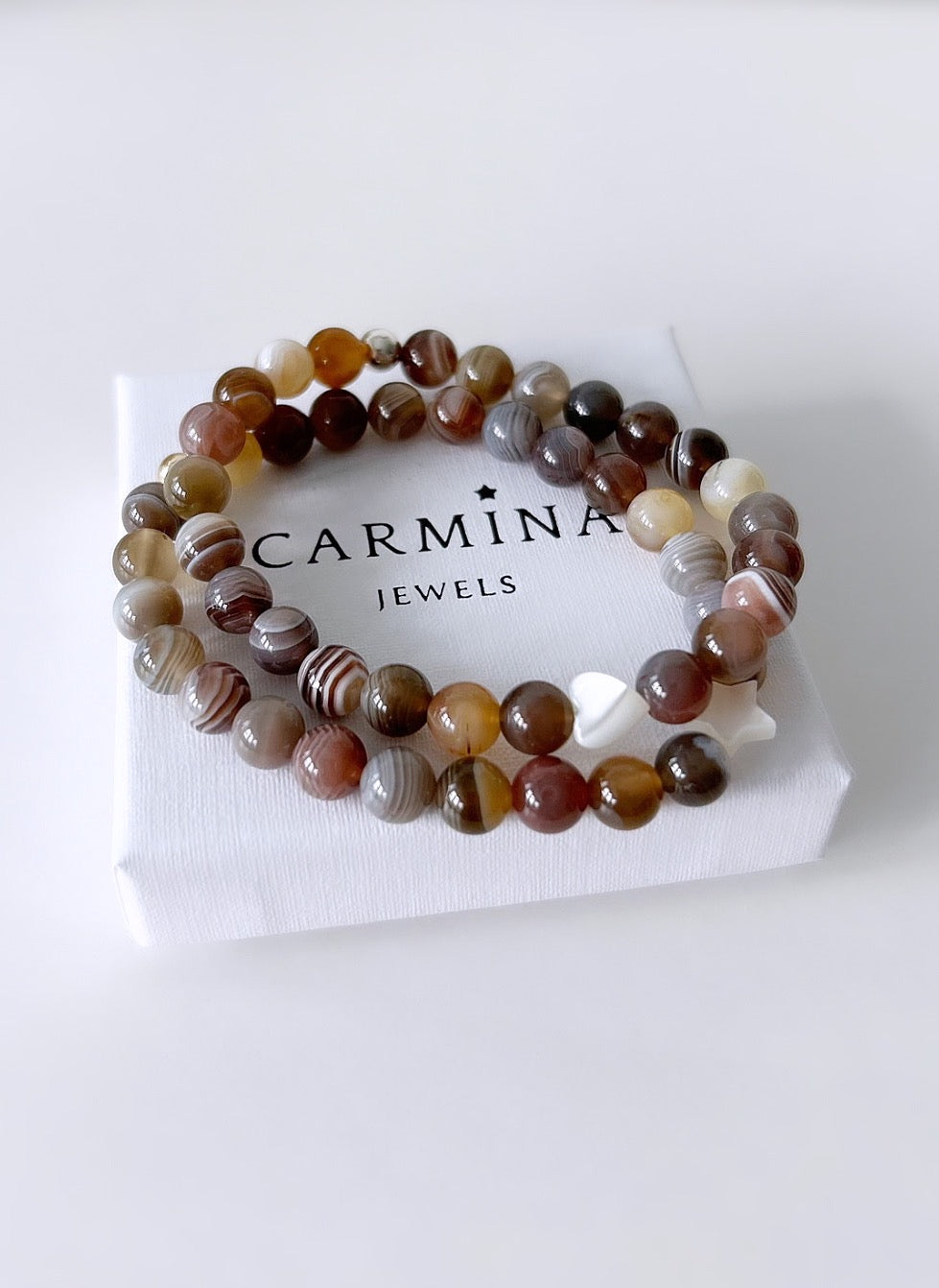 A Botswana agate beaded bracelet with varying shades of brown and white, in a white box with 'Carmina Jewels' branding.