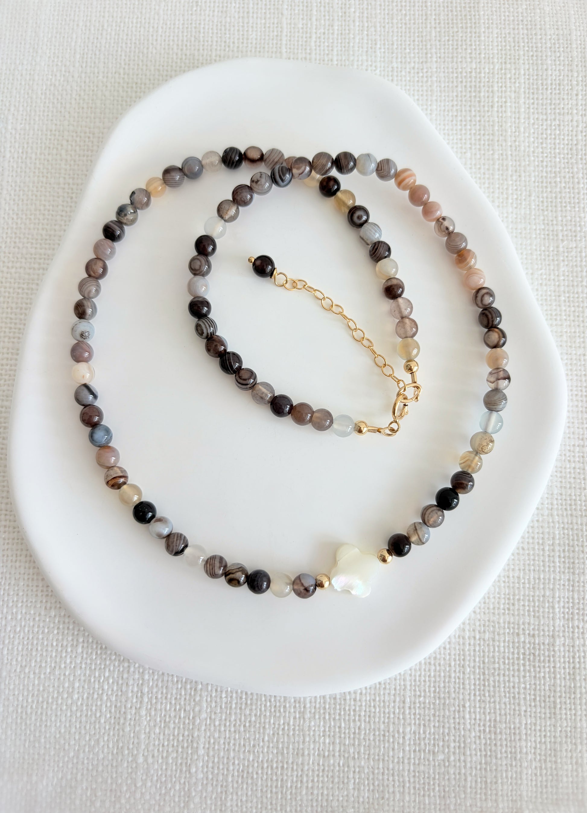 A beautiful Semi precious beaded Botswana Agate necklace with a central Mother of Pearl clover bead. 

Crafted with high quality semi precious beads, each one as beautiful as it is unique.

Available with a choice of either a Sterling Silver or Gold filled clasp. The necklace length is 16” with an 2” extender, finished at the end with a precious bead. 