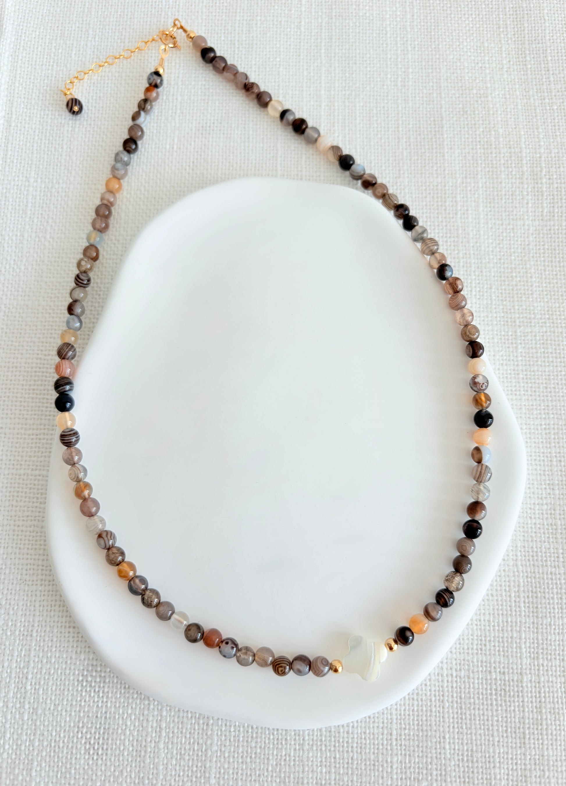 A beautiful Semi precious beaded Botswana Agate necklace with a central Mother of Pearl clover bead. 

Crafted with high quality semi precious beads, each one as beautiful as it is unique.

Available with a choice of either a Sterling Silver or Gold filled clasp. The necklace length is 16” with an 2” extender, finished at the end with a precious bead. 