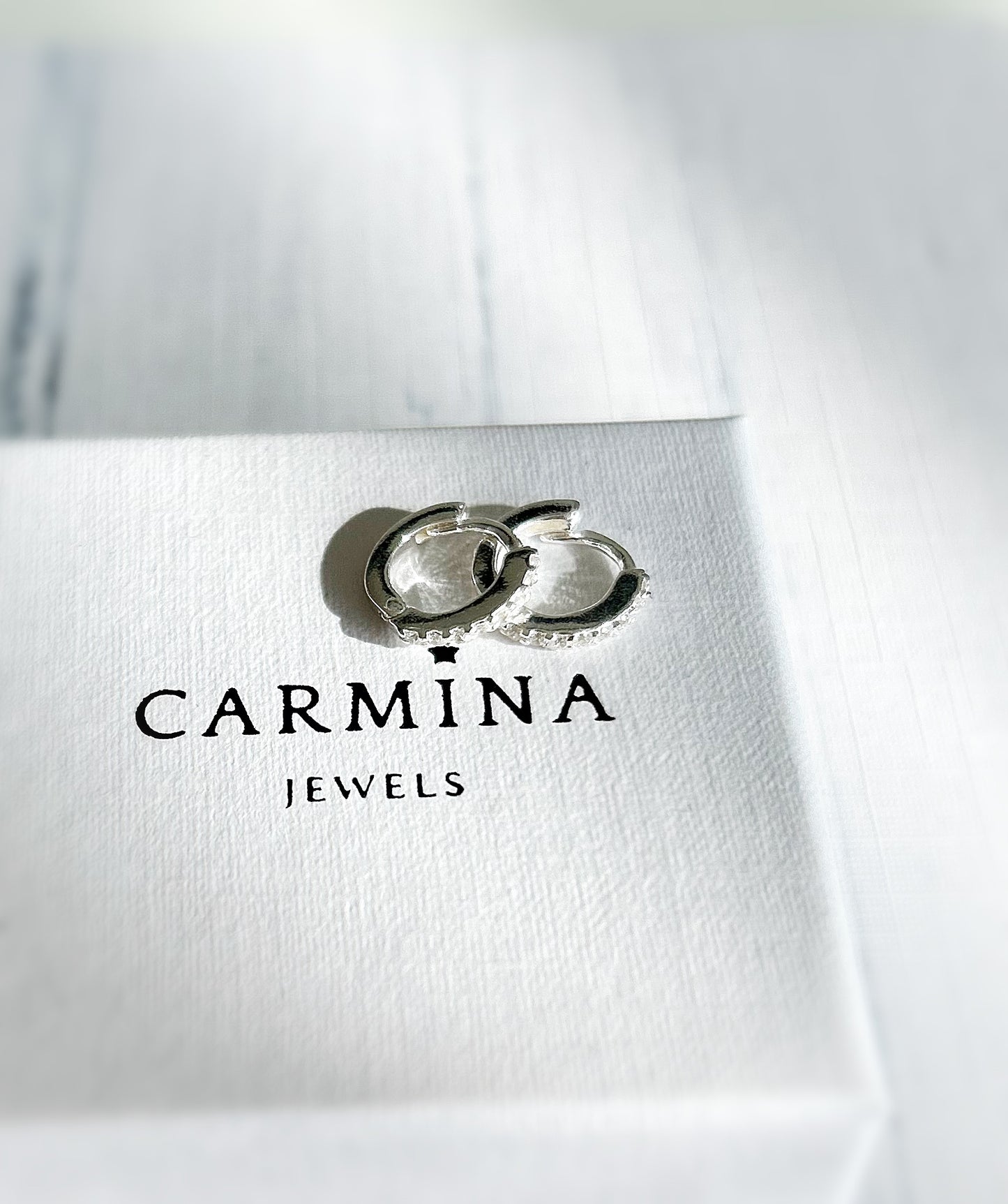 A pair of sterling silver huggie hoop earrings dotted with CZ crystals. 