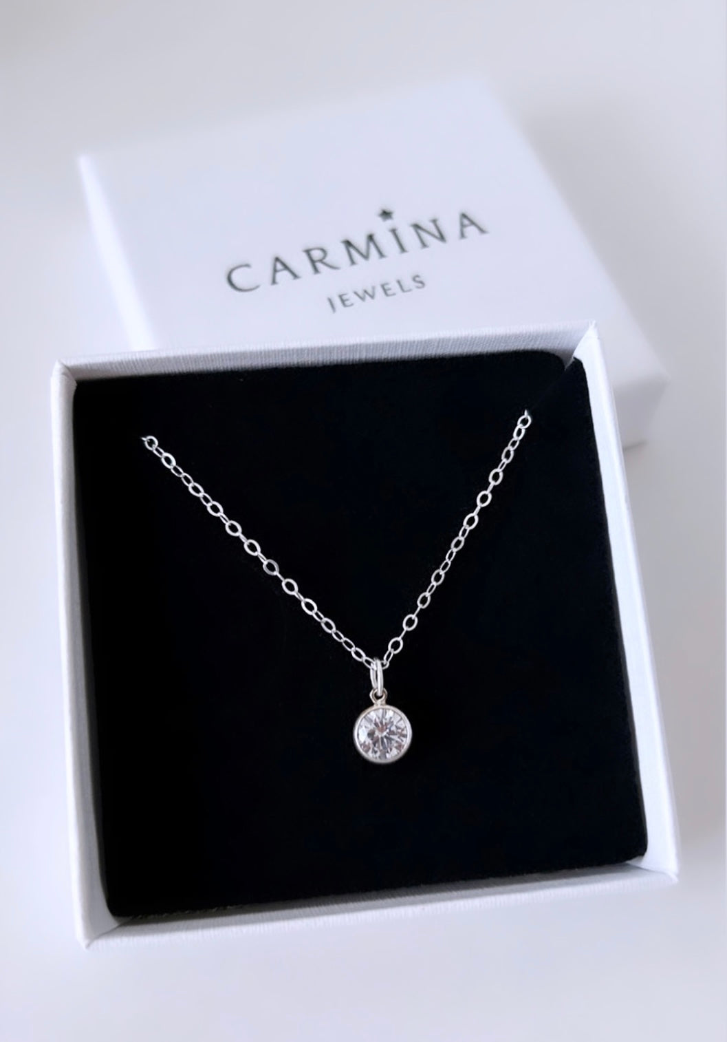 A crystal gemstone pendant necklace with a silver chain and a cubic zirconia charm, presented in a Carmina Jewels box.