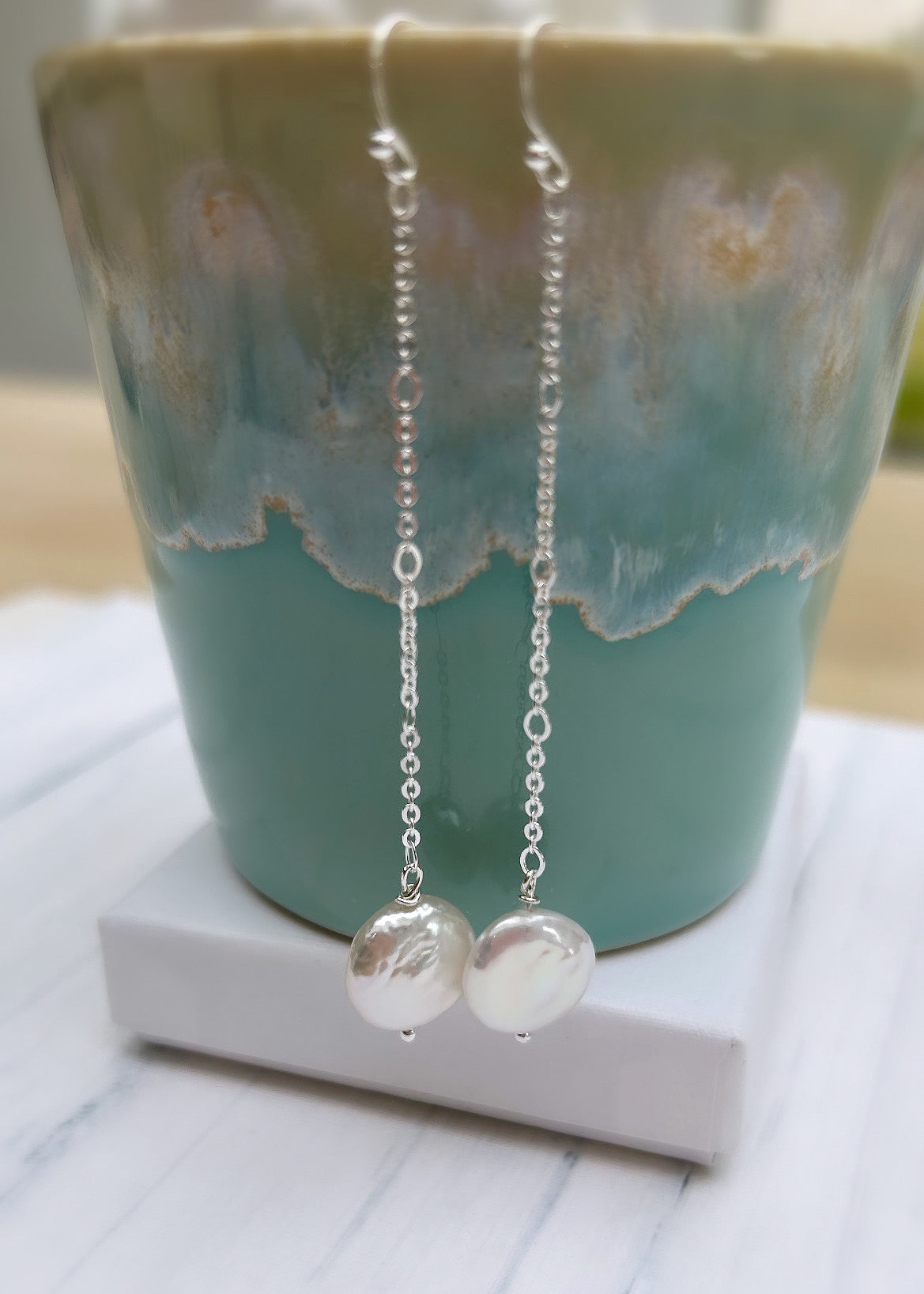 Beautiful dangle pearl earrings with coin shaped Freshwater Pearls. The earrings are on a hook ear fastening with the pearls hanging from a delicate Sterling Silver figaro chain.