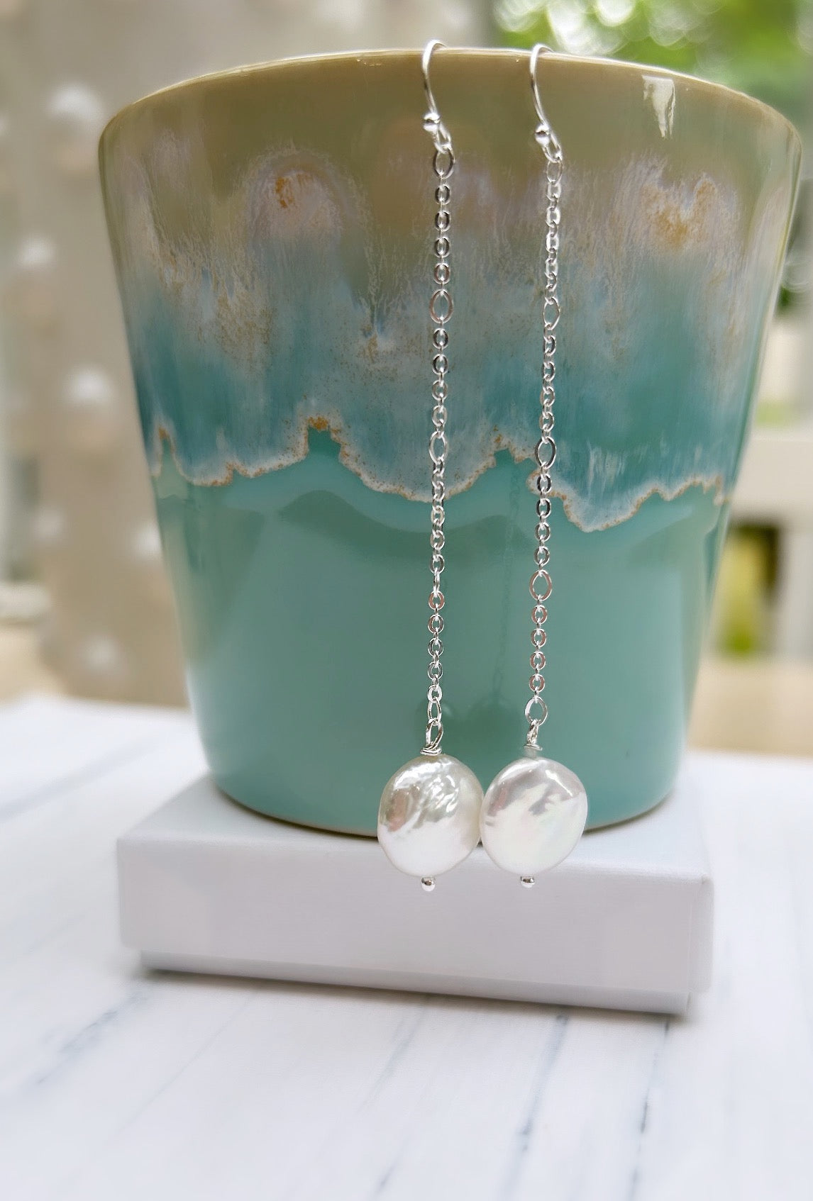 A pair of dangle pearl earrings with a coin-shaped freshwater pearl, attached to a delicate sterling silver figaro chain