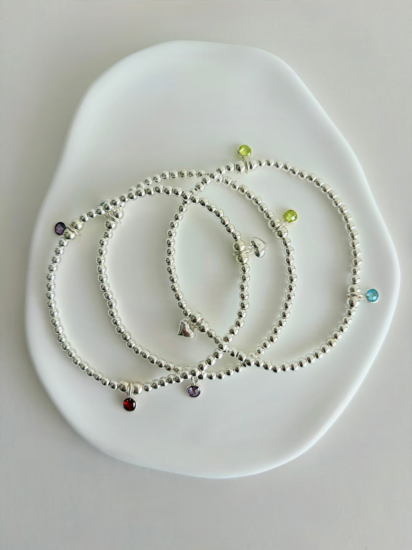 A sterling silver or gold filled beaded bracelet with a crystal birthstone charm. Additional charms can be added to represent family members or loved ones 