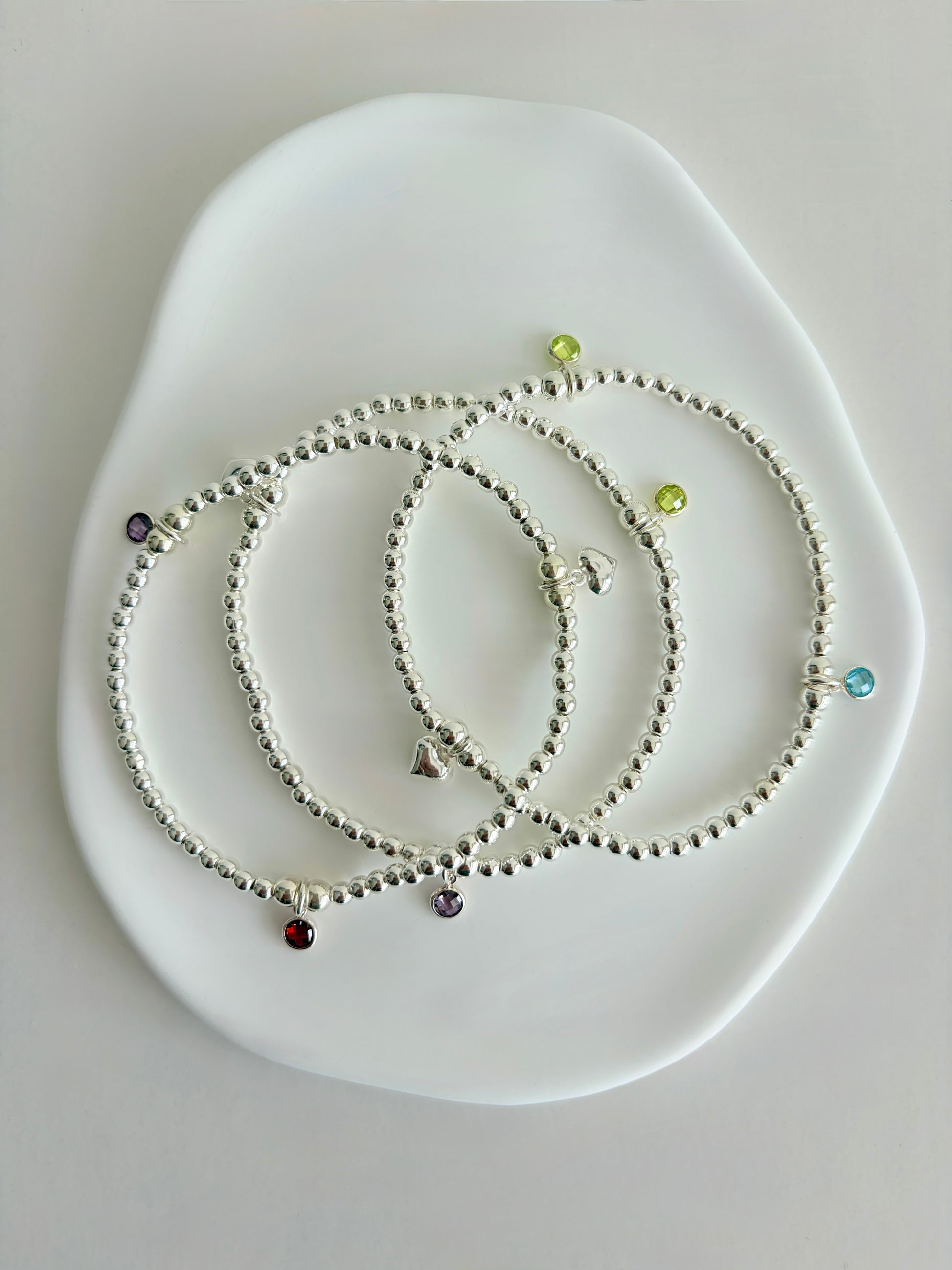A sterling silver or gold filled beaded bracelet with a crystal birthstone charm. Additional charms can be added to represent family members or loved ones 