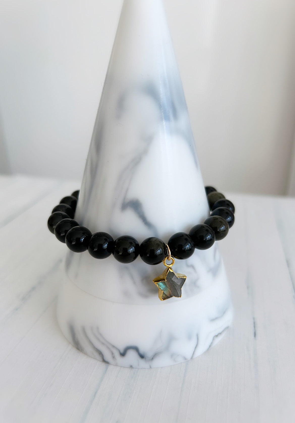 A black beaded bracelet with a gold-colored labradorite stone star-shaped charm
