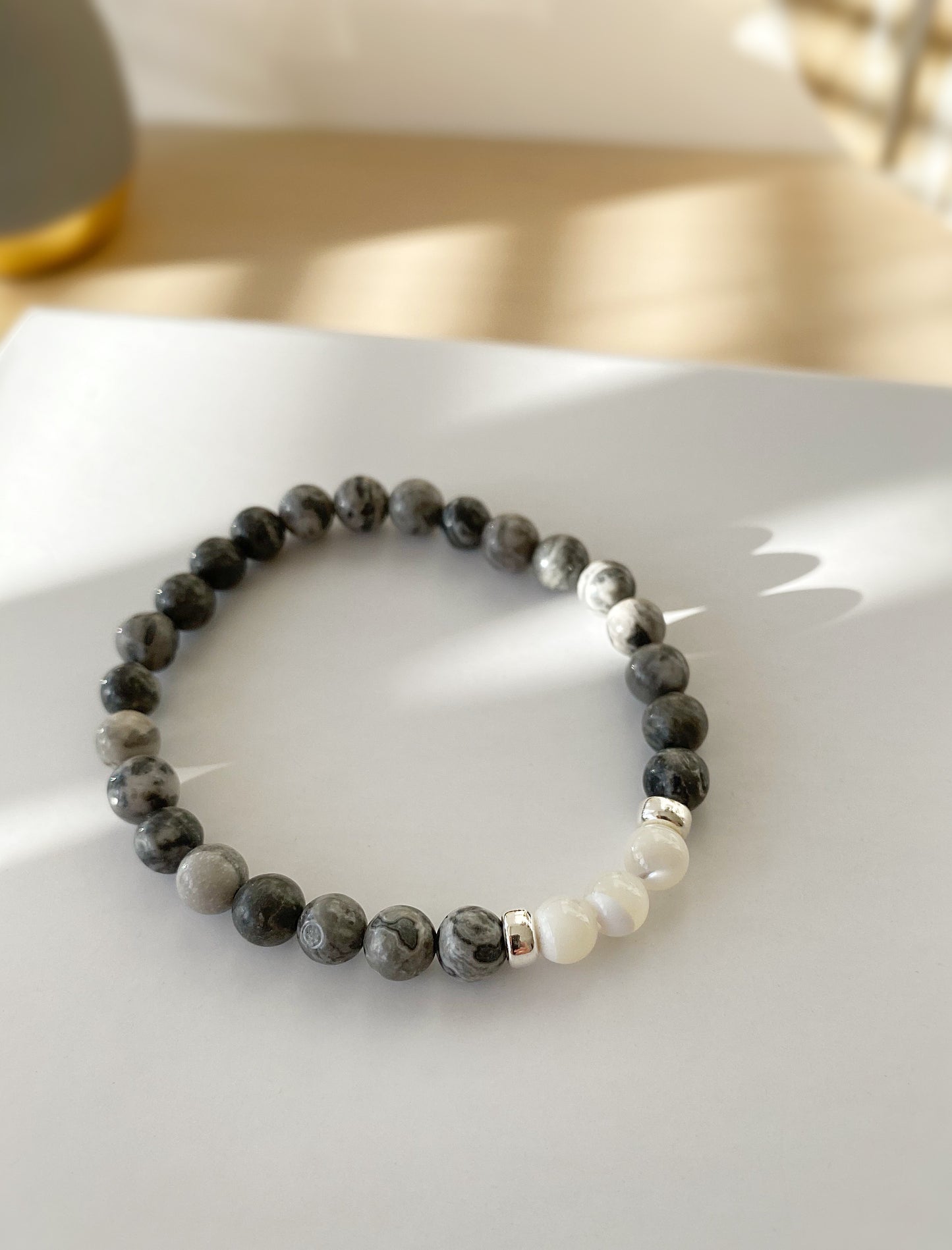 A beaded bracelet with a mix of grey jasper and mother of pearl beads, finished with sterling silver doughnut spacer beads