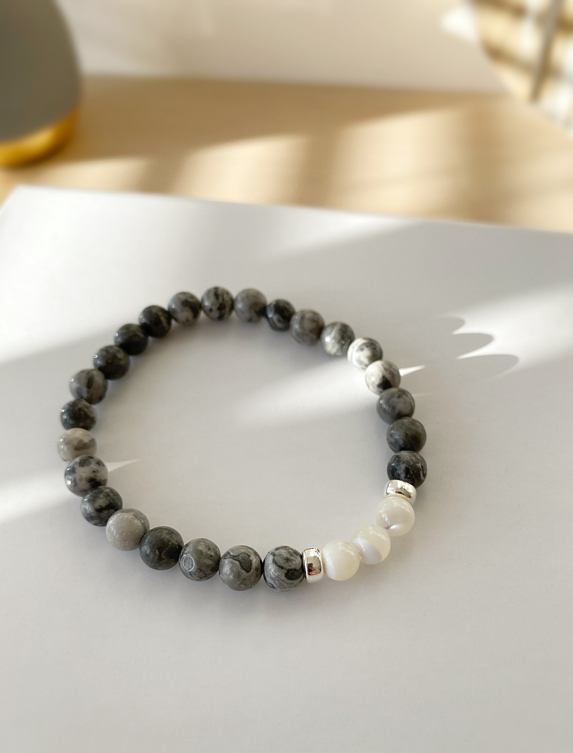 A beaded bracelet with a mix of grey jasper and mother of pearl beads, finished with sterling silver doughnut spacer beads