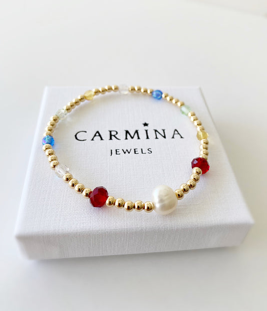 A gold-colored bracelet with blue, red, and white glass beads, featuring a central baroque freshwater pearl, presented in a white box with 'CARMINA JEWELS' branding.