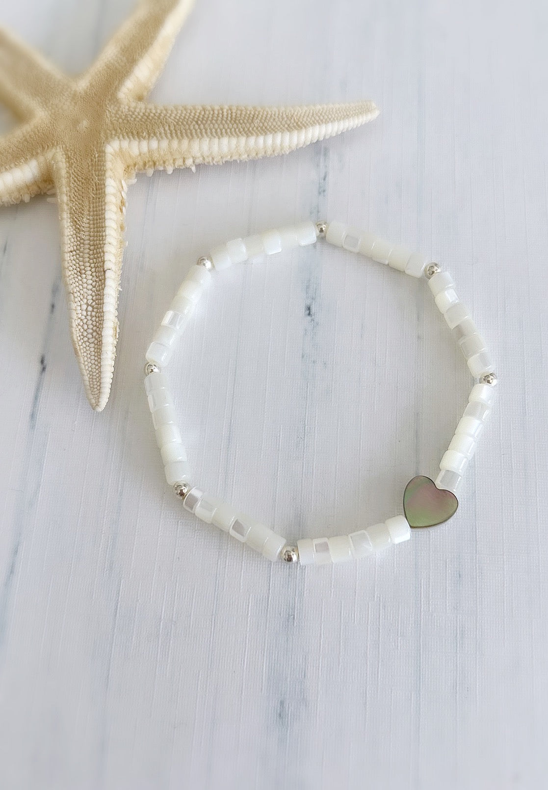 A Mother of Pearl bead bracelet with a heart-shaped bead in the center, featuring a pearlescent finish and Sterling Silver spacer beads