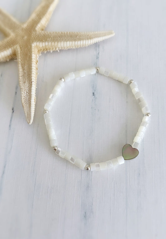 A Mother of Pearl bead bracelet with a heart-shaped bead in the center, featuring a pearlescent finish and Sterling Silver spacer beads
