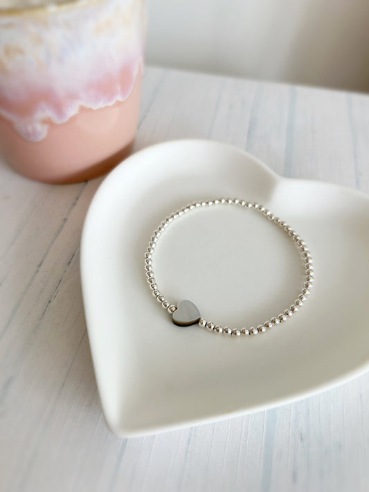 A silver beaded bracelet with a single pearl heart charm