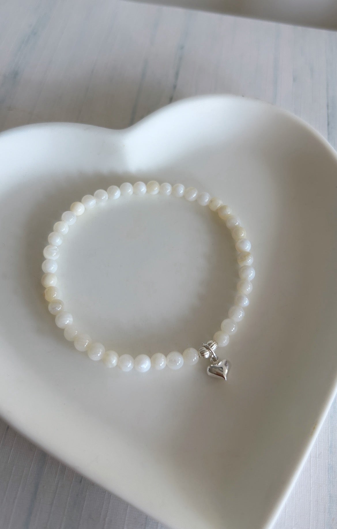 A beautiful Mother of Pearl beaded bracelet, with a mini puff heart charm, hand threaded on high quality jewellery elastic for a comfortable stretch fit. Available with either a Gold vermeil or Sterling Silver finish.