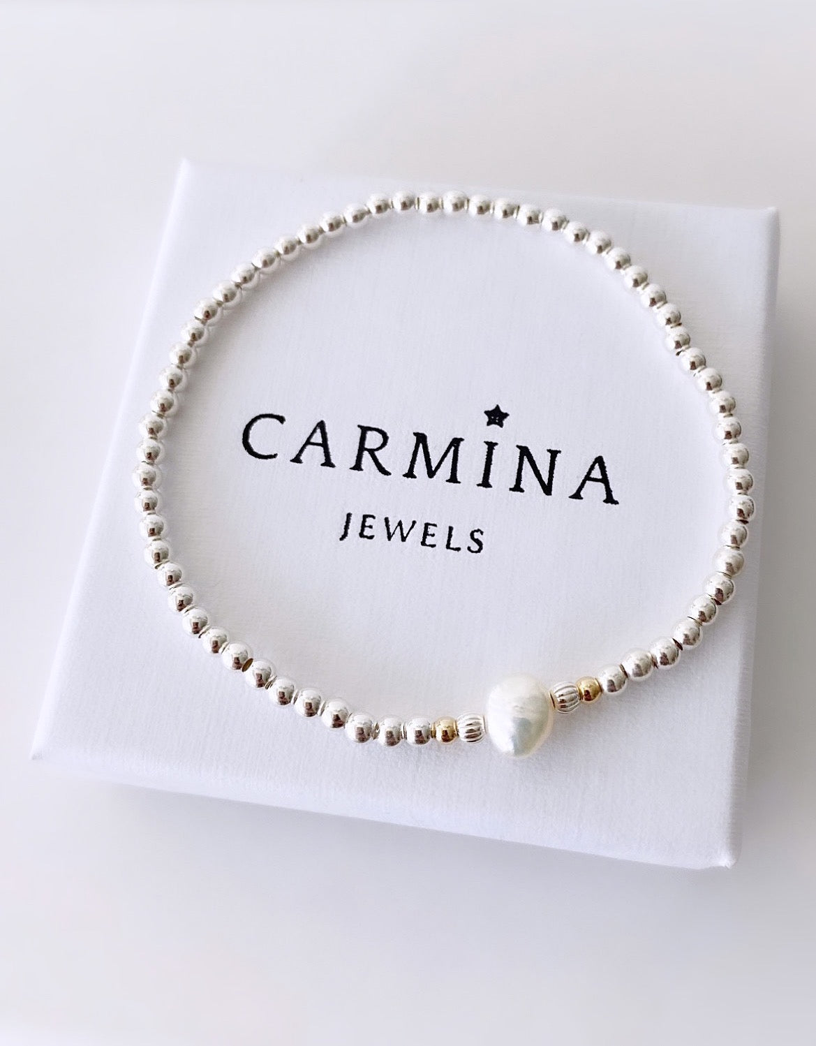 A sterling silver beaded bracelet with a central baroque Freshwater pearl, threaded on a stretch cord, with gold filled and silver corrugated beads, presented in a white box with 'CARMINA JEWELS' branding.