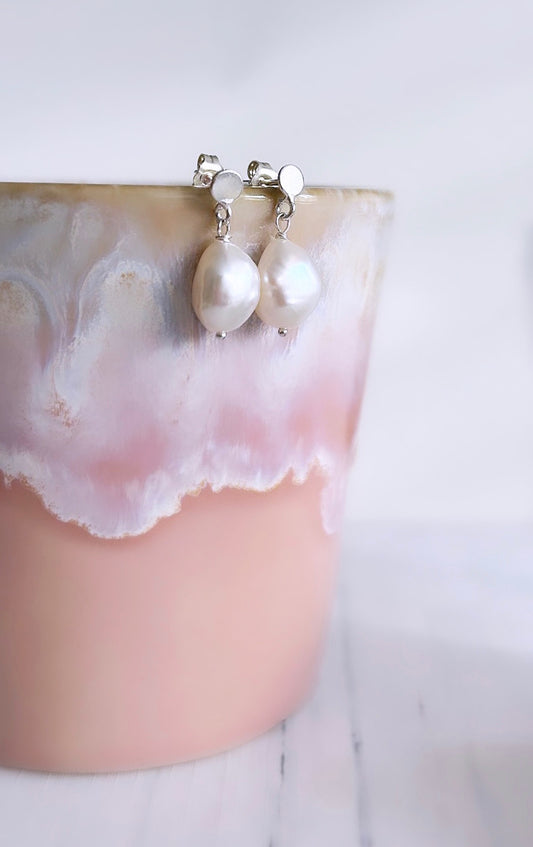 A pair of pearl droplet stud earrings dangling from a sterling silver mini disc ear stud, with butterfly clasp fastenings