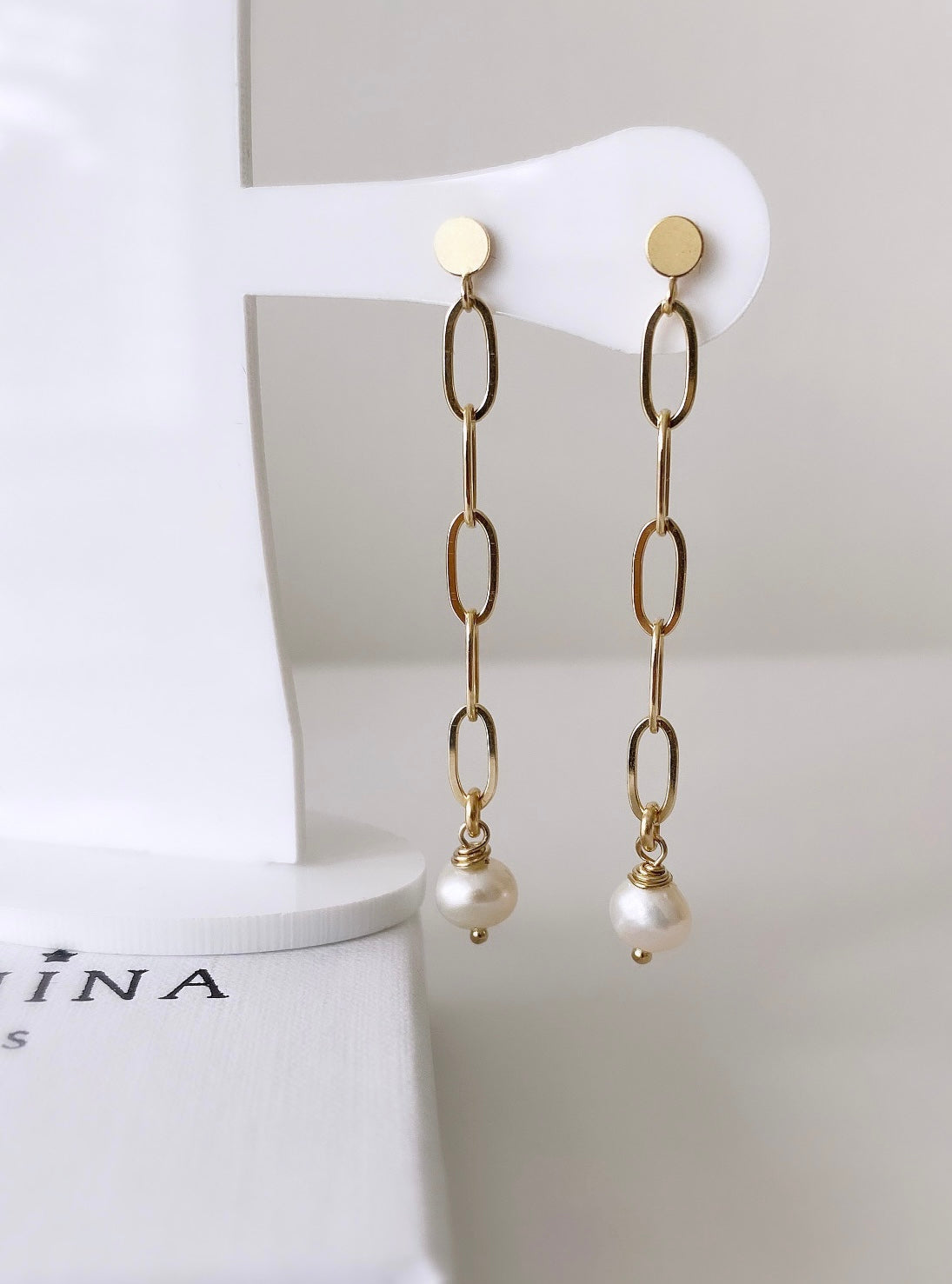 A pair of gold-colored pearl drop earrings  with the earrings featuring large link chains and baroque freshwater pearls.