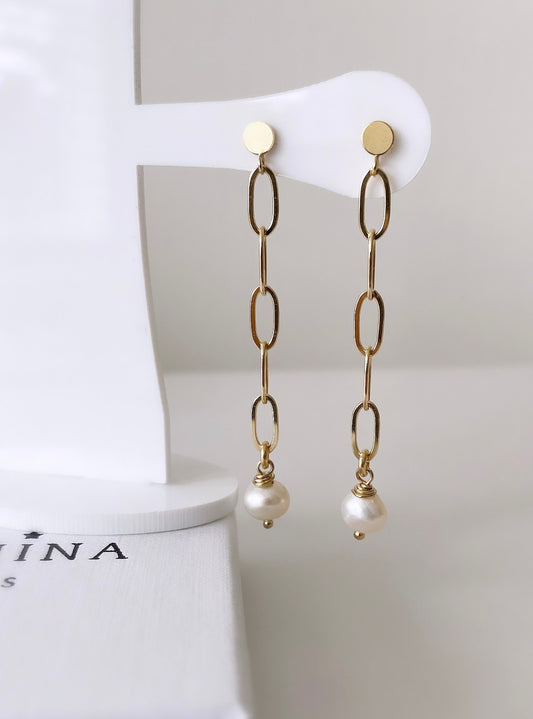 A pair of gold-colored pearl drop earrings  with the earrings featuring large link chains and baroque freshwater pearls.