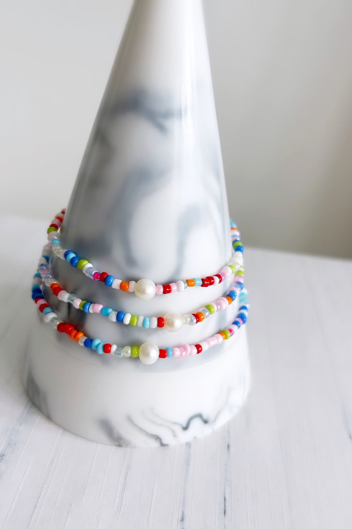 A multicolored beaded bracelet or anklet with a central white freshwater pearl, displayed