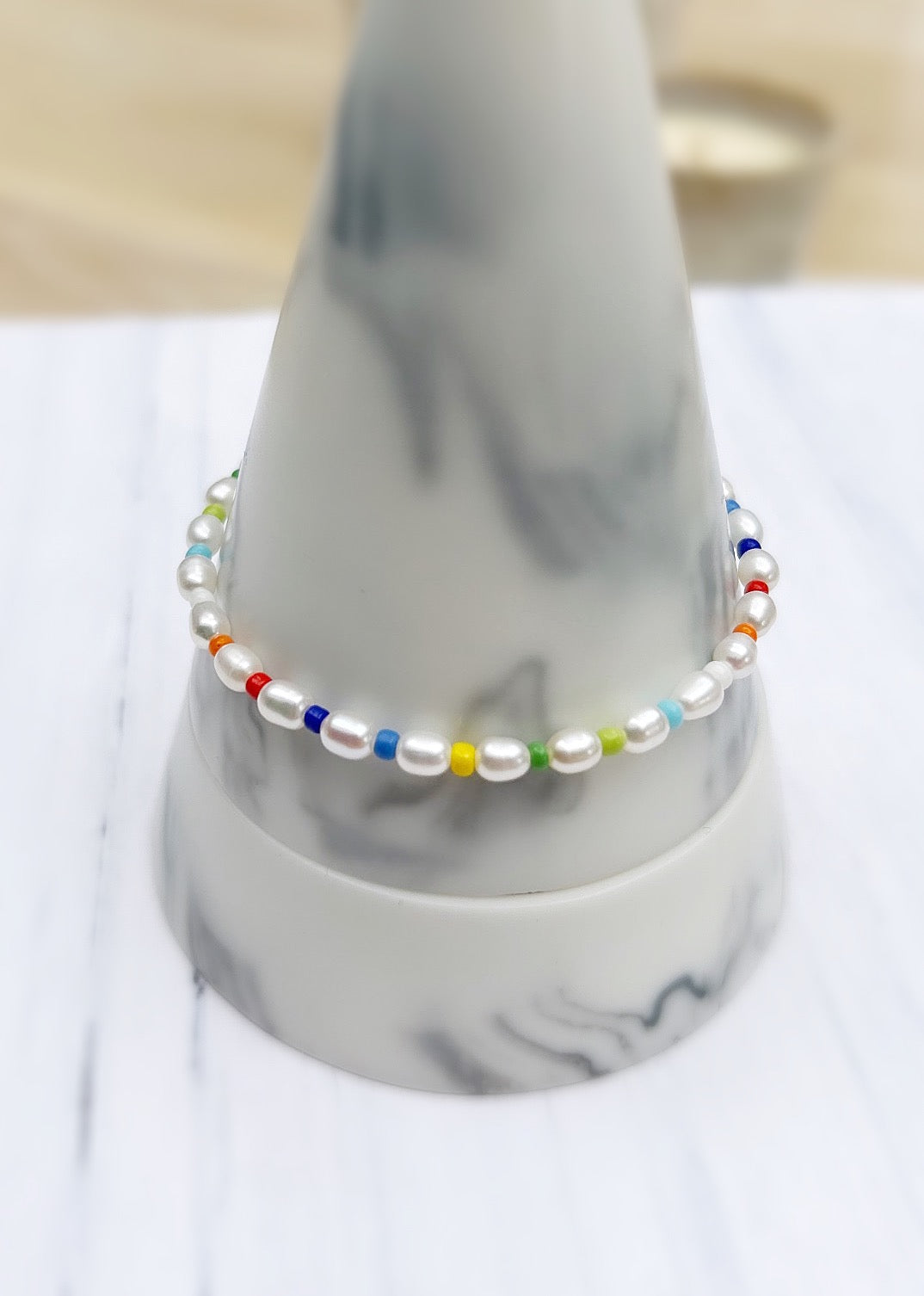 A rice pearl bracelet with a variety of colorful glass seed beads, displayed on a marble surface.