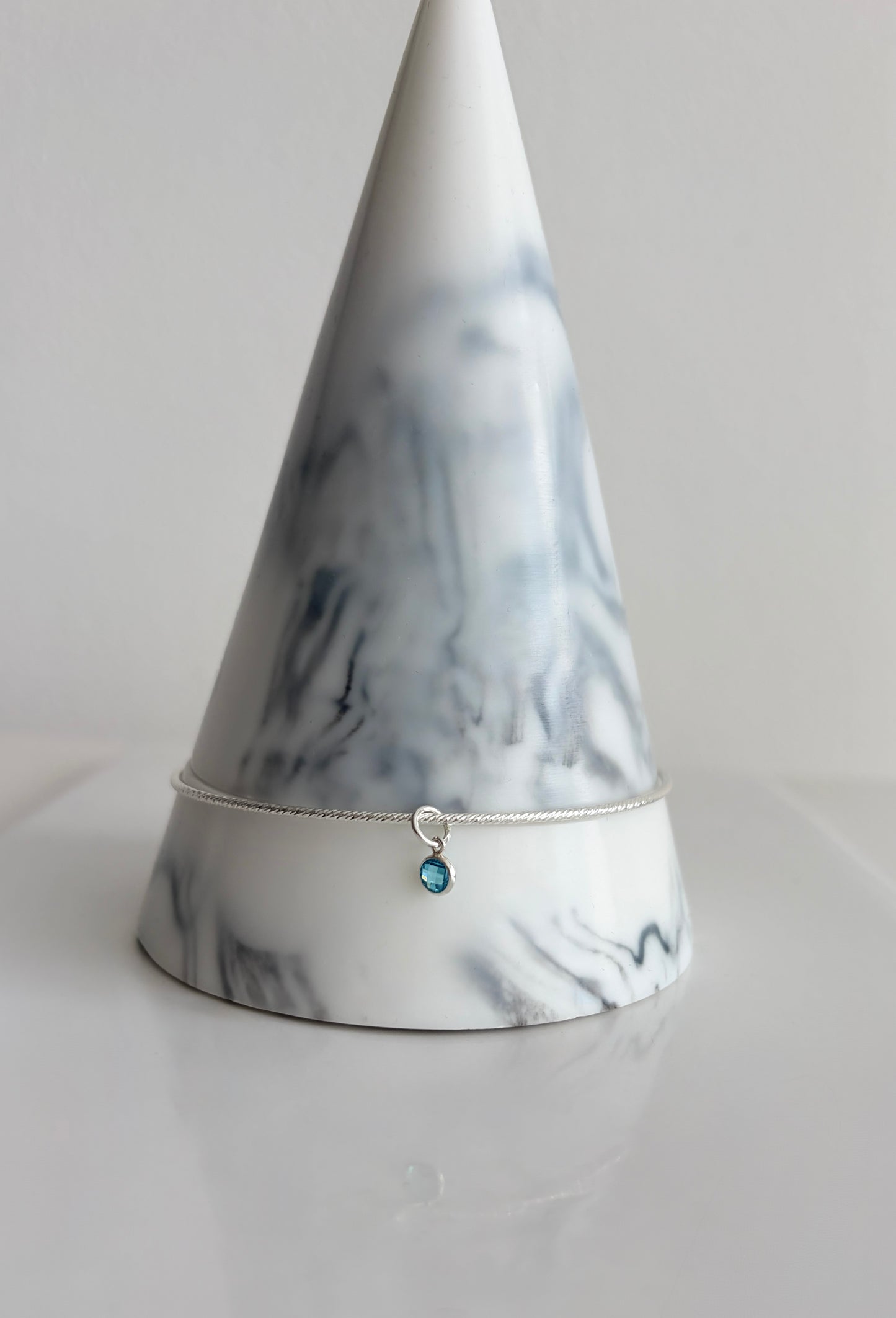 A beautiful Sterling Silver bangle, made with a sparkle finish adorned with your choice of a single crystal Birthstone charm  