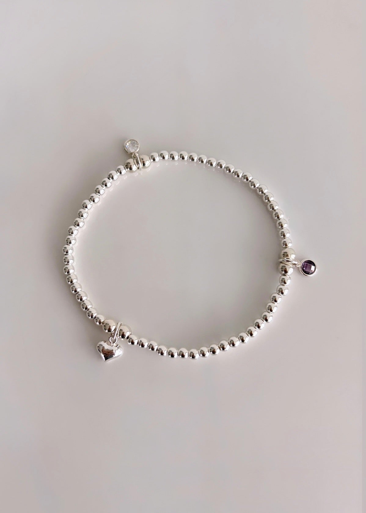 A sterling silver or gold filled beaded bracelet with a crystal birthstone charm. Additional charms can be added to represent family members or loved ones 