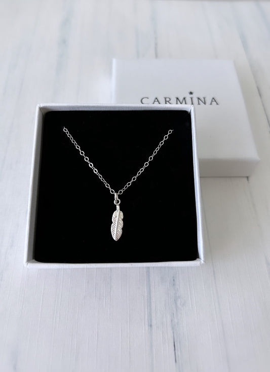 A silver feather pendant necklace in a gift box with 'Carmina' branding.