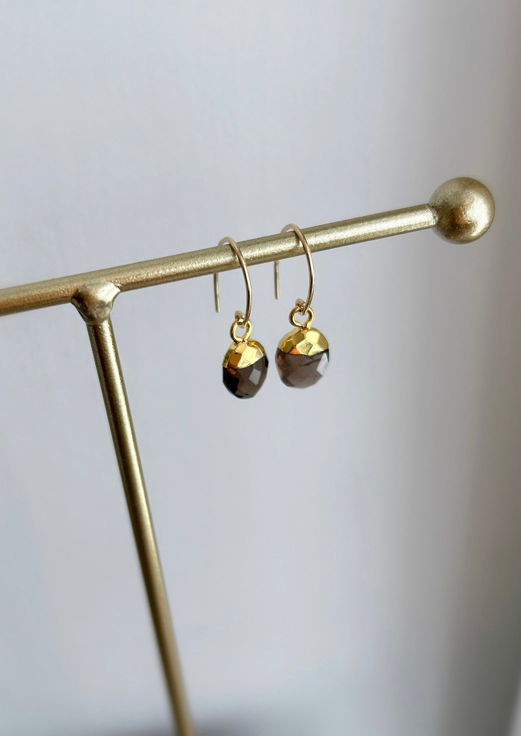 A pair of Smoky Quartz gemstone earrings attached to a gold-colored curved ear wire 