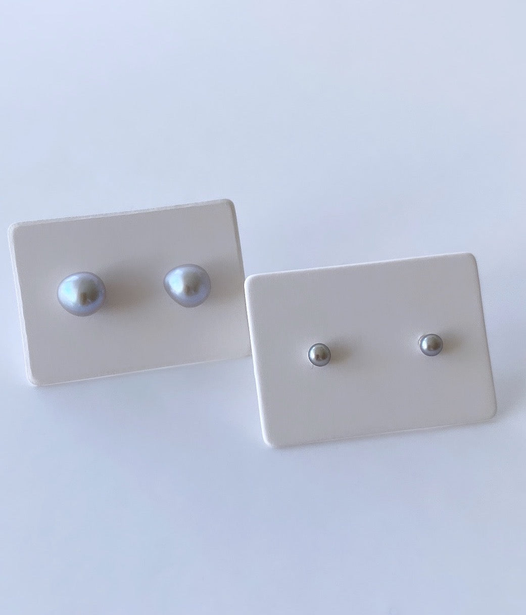 A pair of tiny button pearl stud earrings on white sterling silver posts with silver butterfly clasps.