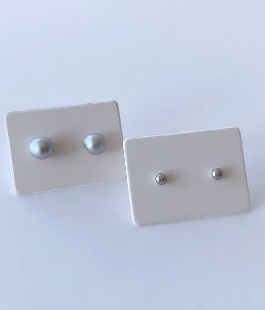 A pair of tiny button pearl stud earrings on white sterling silver posts with silver butterfly clasps.