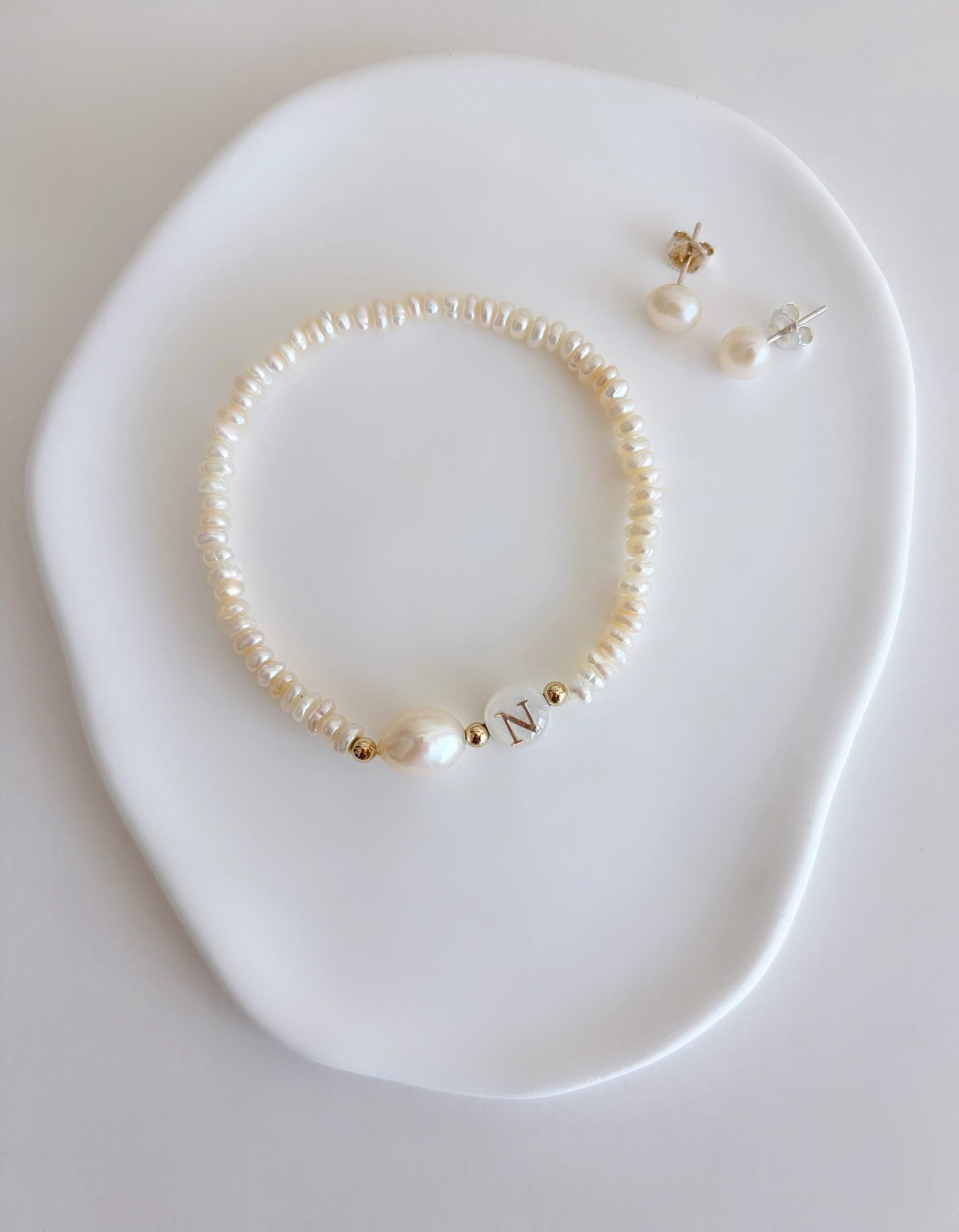 A delicate personalised stacking bracelet featuring a large baroque Pearl and a mother of pearl bead with your choice of initial. The bracelet is hand threaded with tiny off white Freshwater Pearls on a stretch cord, finished with a choice of either Sterling Silver or Gold filled spacer beads ~ a perfect stacker! 
