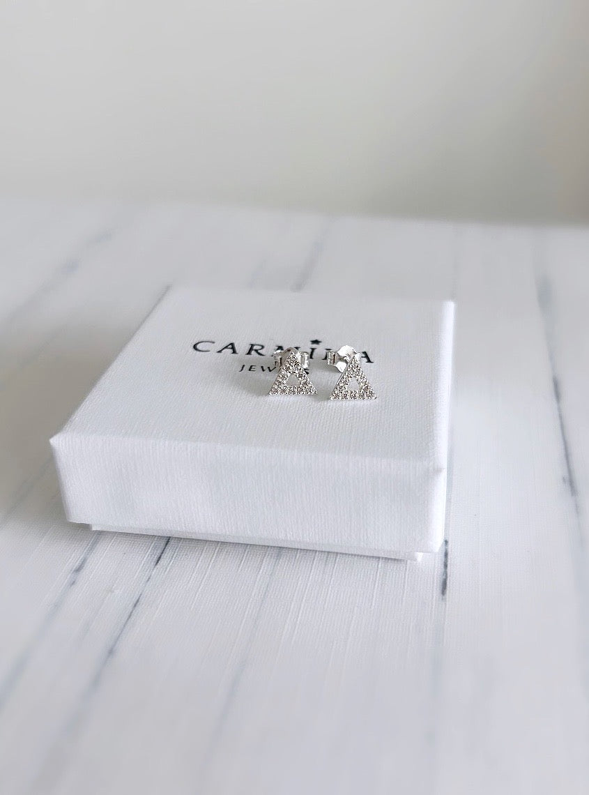A pair of CZ silver triangle stud earrings in a white gift box with 'Carmina' branding on it.