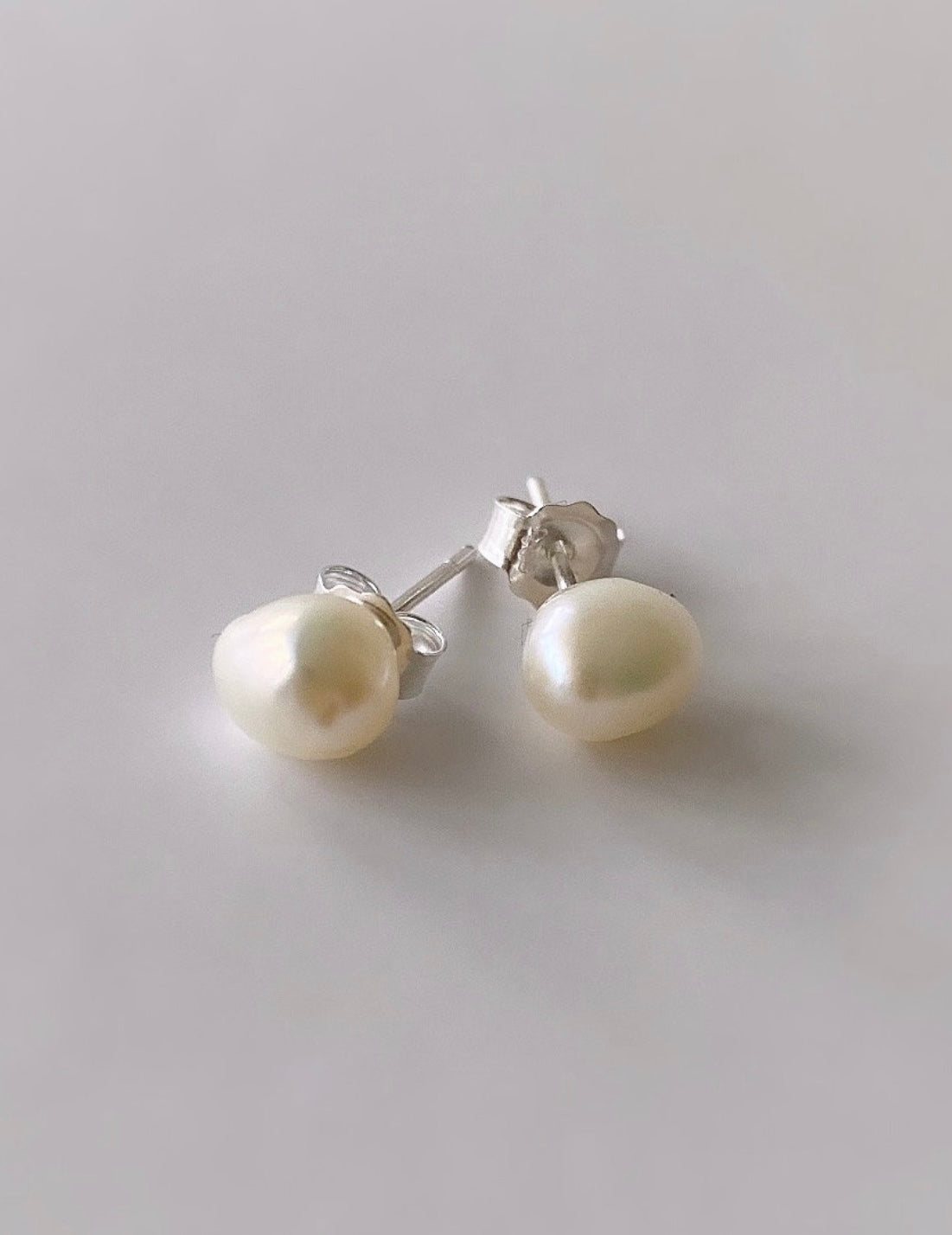 A pair of baroque white pearl stud earrings with silver posts and butterfly clasps 